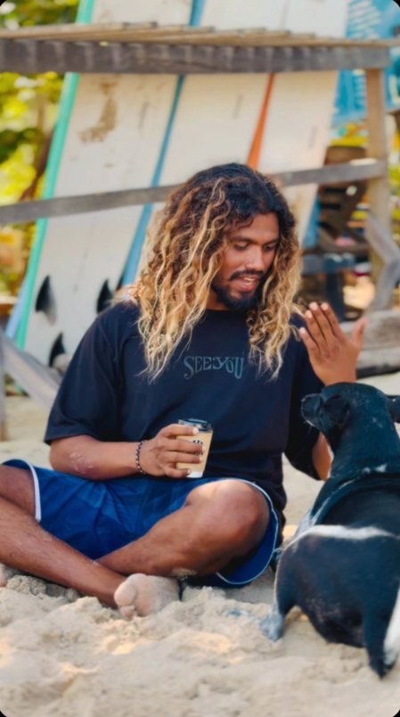 A surfer with a coffee and a beach dog on the sand