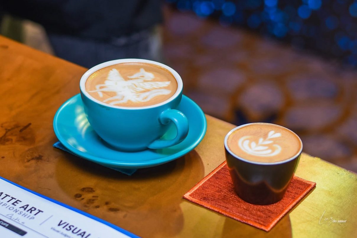 A pegasus latte art cappuccino in a turquoise cup beside a rosetta cortado